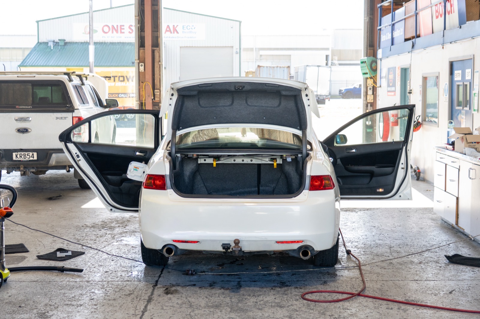 Car with doors, bonnet and boot open in the workshop bay during a full inspection.