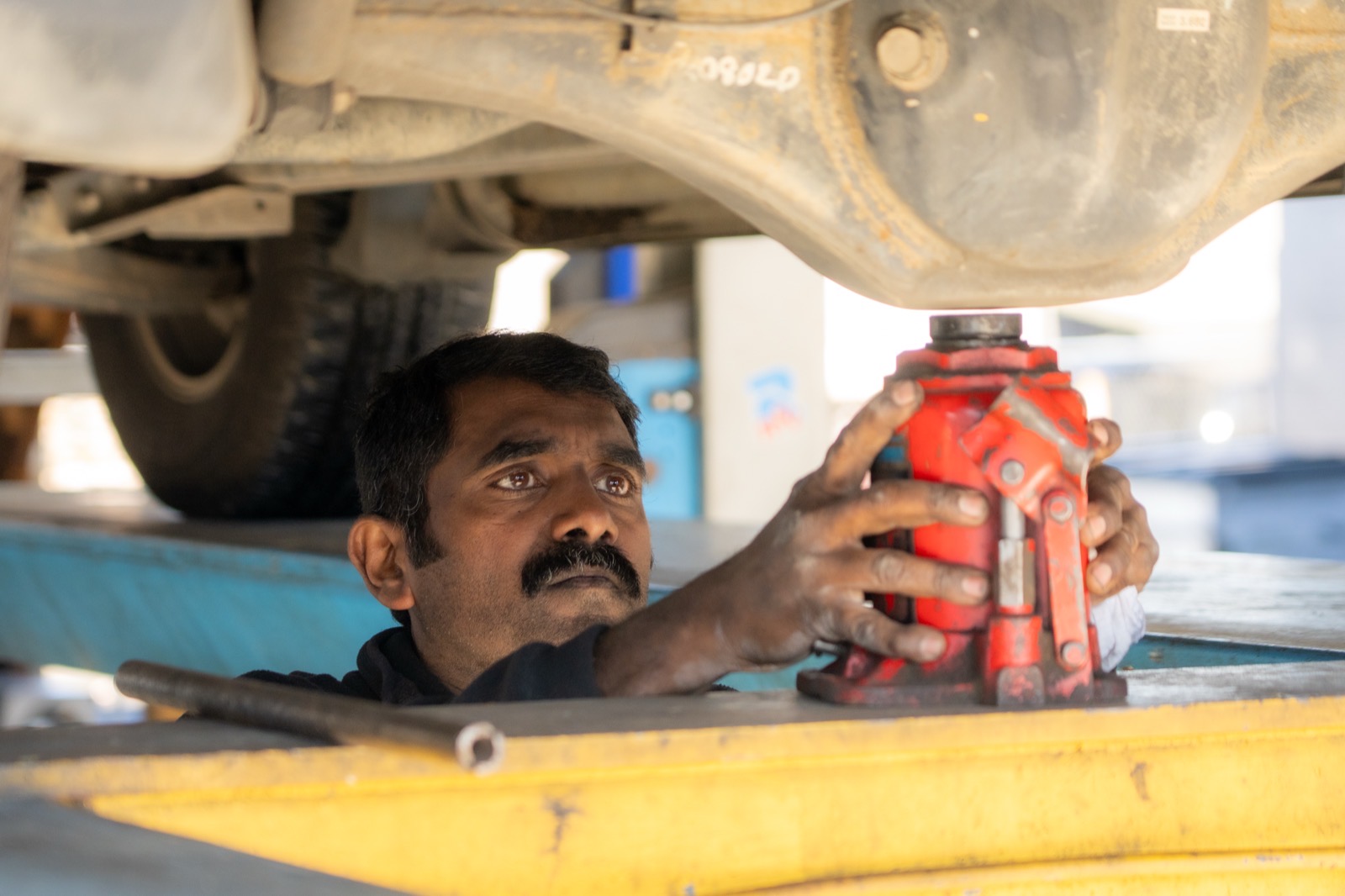 Mechanic positioning a hydraulic jack under the axle of a raised vehicle during suspension work.
