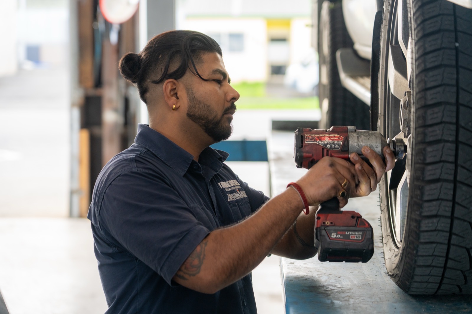 Mechanic removing a wheel with an impact wrench to access the brakes on a hoisted vehicle.